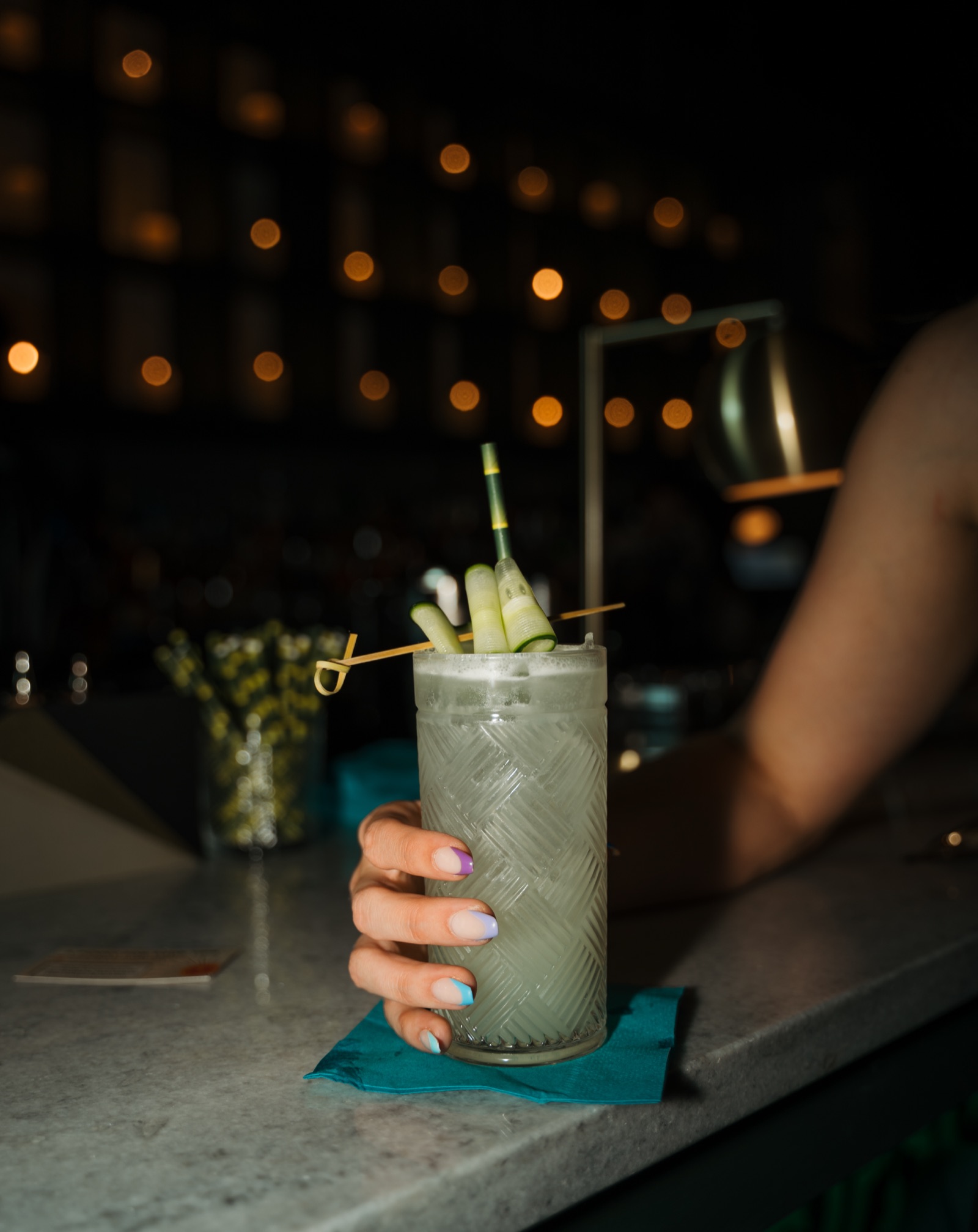 A tall cocktail with cucumber garnish on a bar